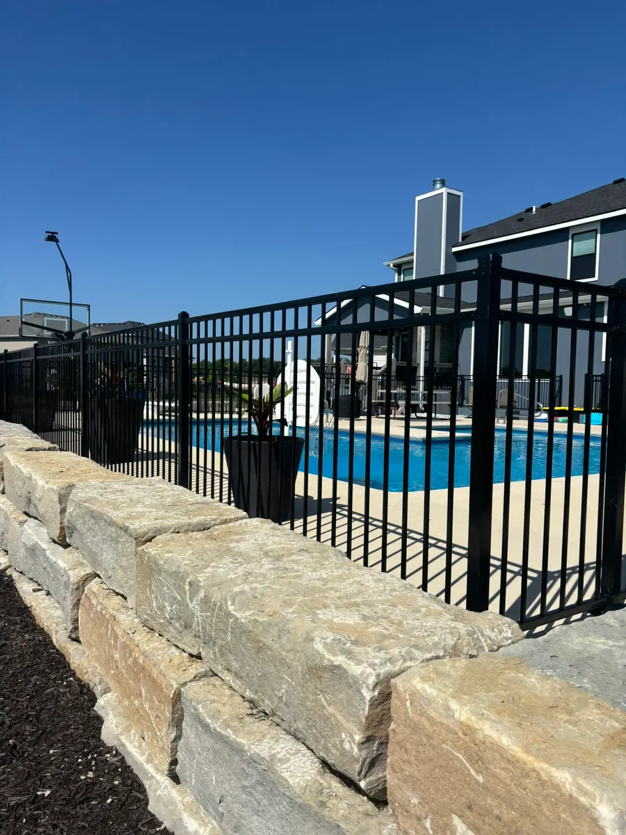 Black aluminum pool fence set above a limestone retaining wall by RKC Wood Care Pros