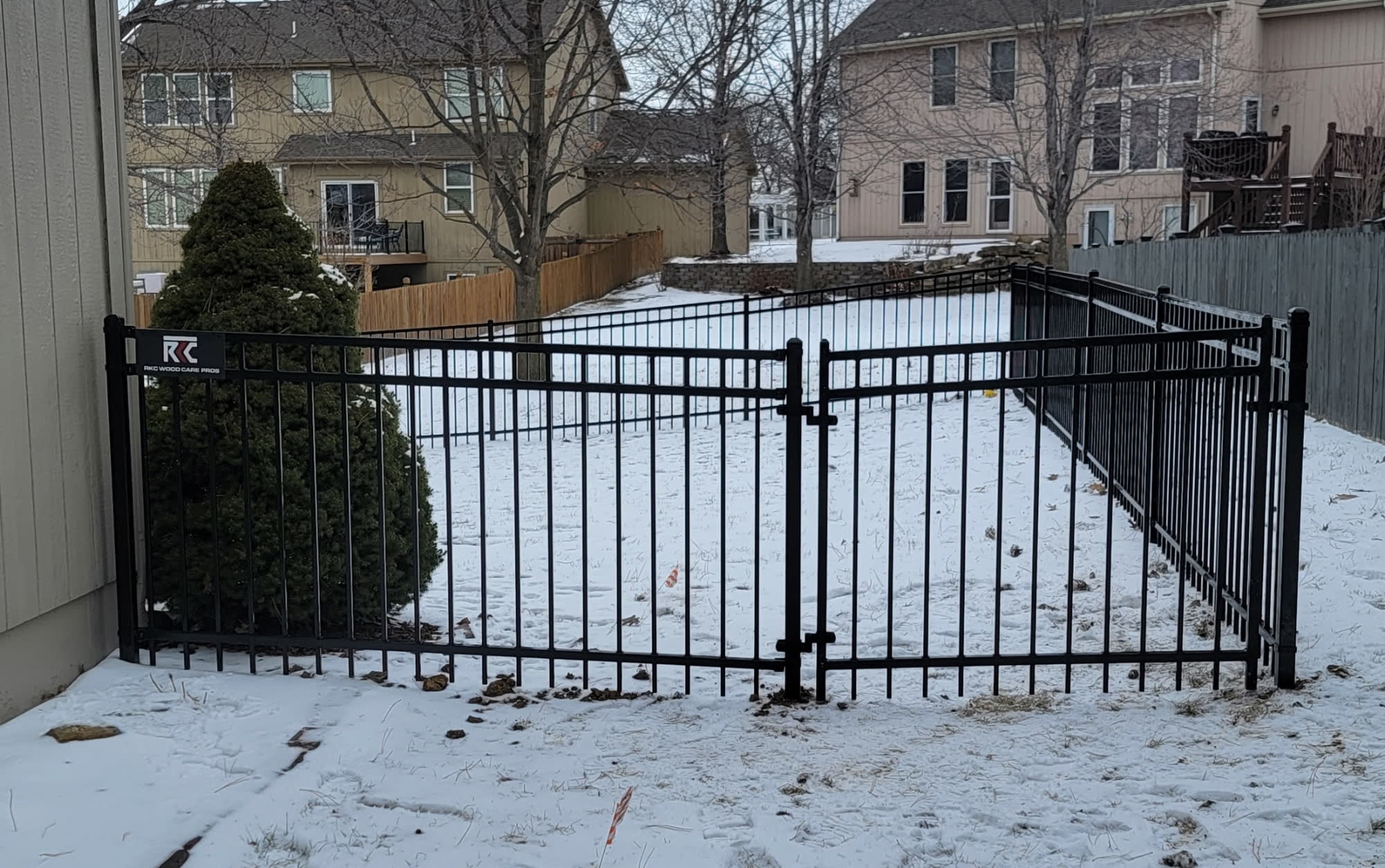 Black aluminum double-drive gate in a snowy Kansas City backyard — RKC Wood Care Pros