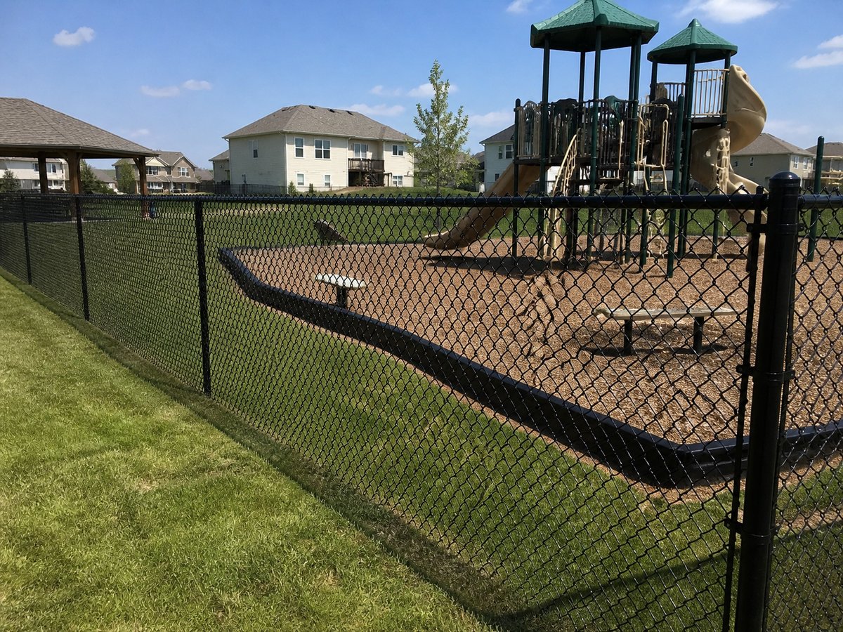 Black vinyl-coated chain link fence around a suburban playground in Kansas City — RKC Wood Care Pros