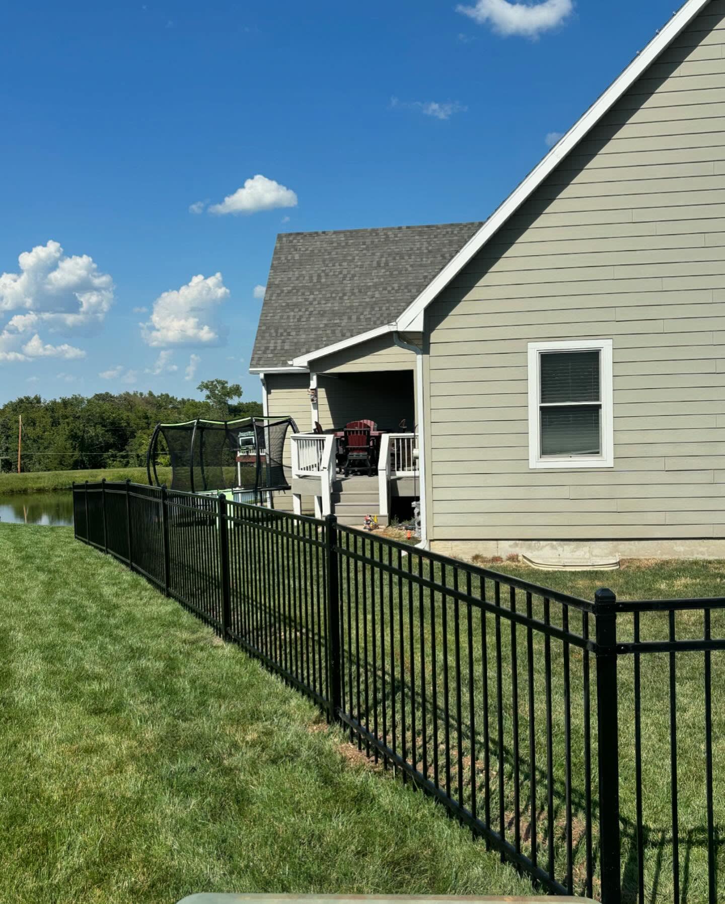 Black powder-coated ornamental fence with flat-top pickets in a backyard near a pond — RKC Wood Care Pros