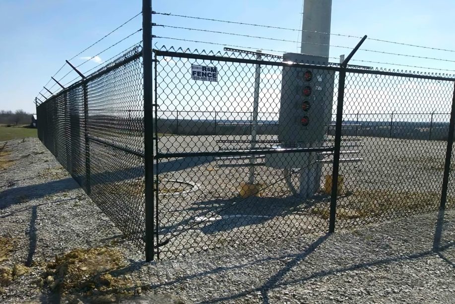 Black vinyl-coated chain link fence with three-strand barbed wire at a utility substation — RKC Wood Care Pros