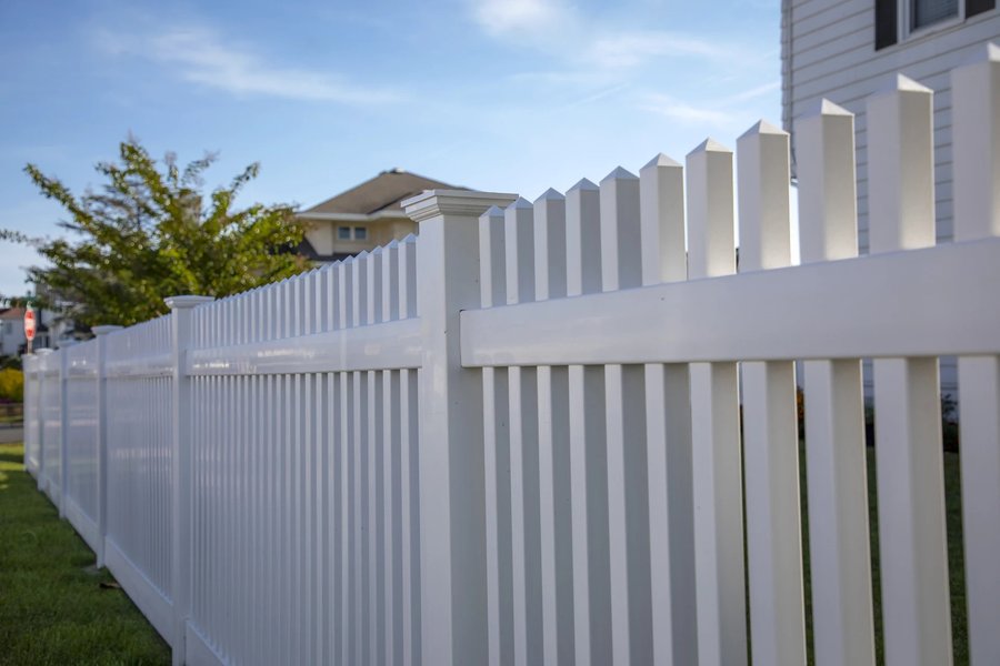 White vinyl spaced picket fence with pointed tops along a suburban front yard — RKC Wood Care Pros