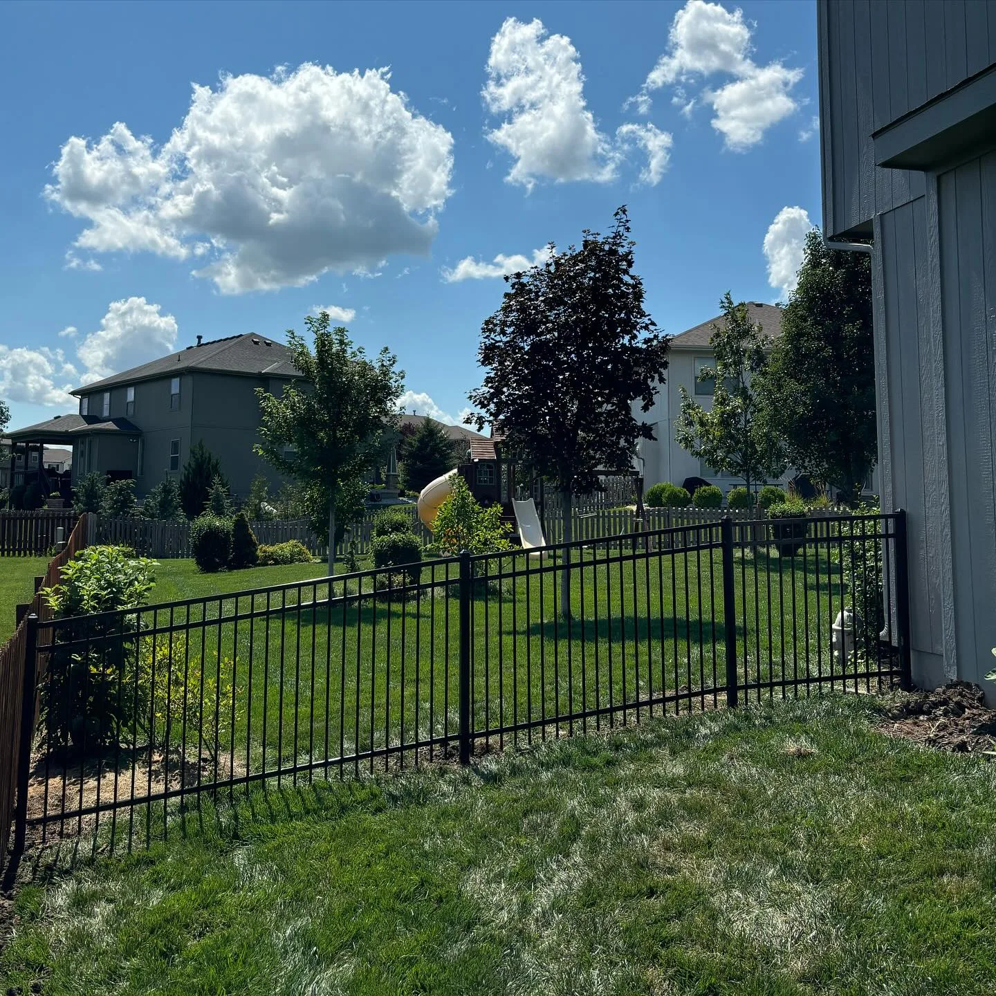 Short black ornamental aluminum fence defining backyard boundary in Leawood, KS on a sunny day