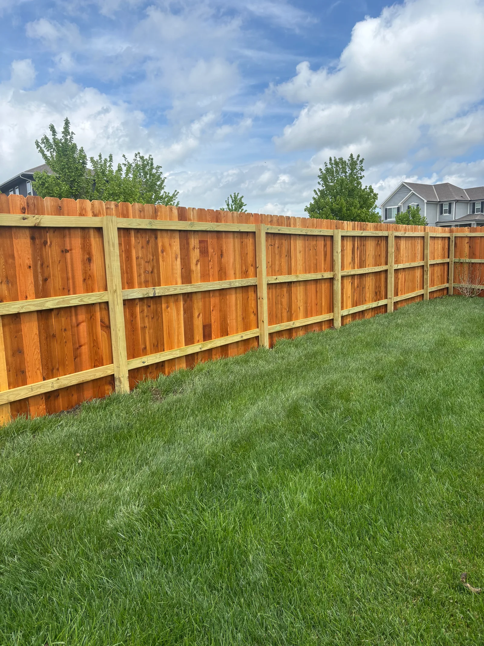New cedar privacy fence running along a large lot in Blue Springs, MO on a partly cloudy spring day