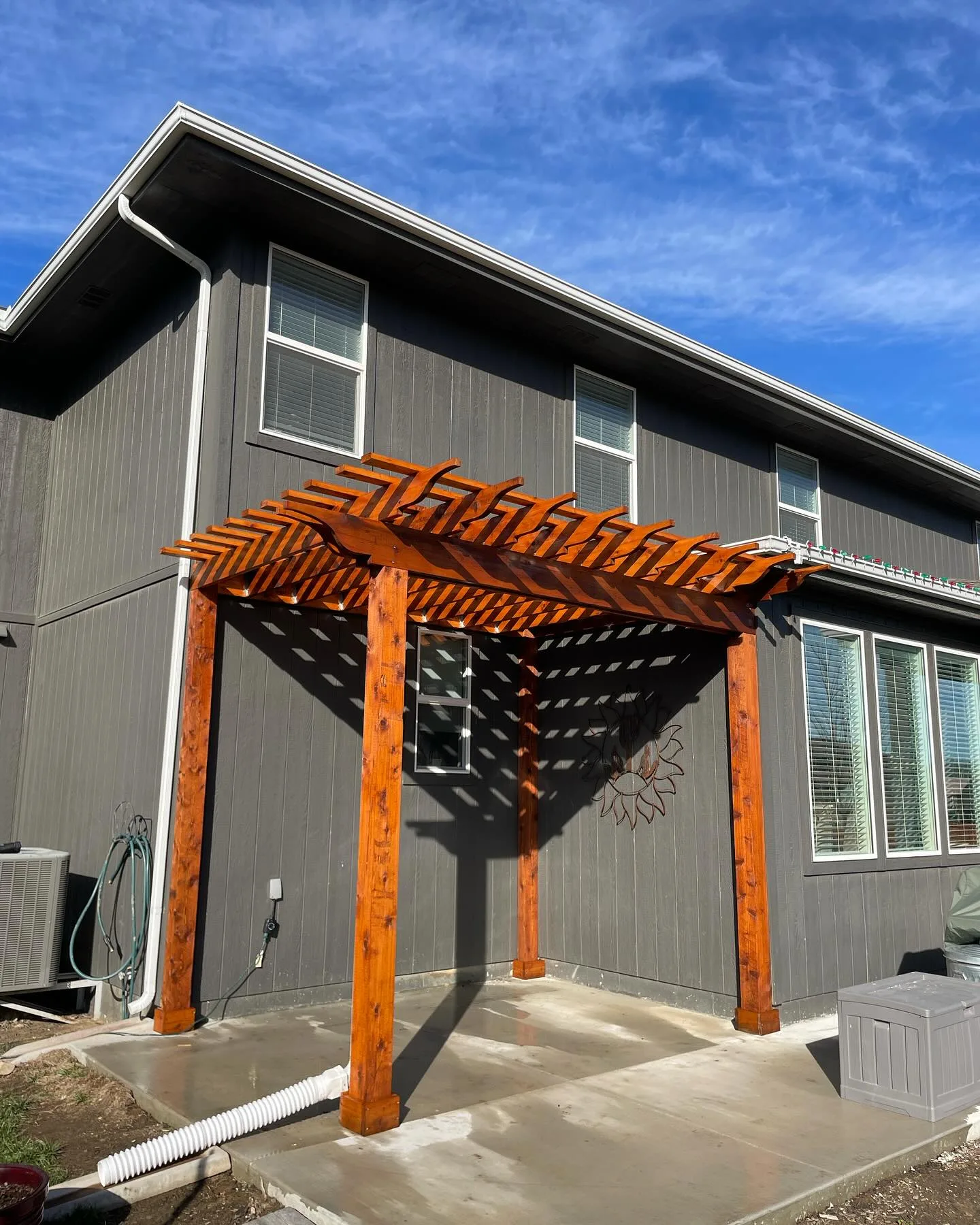 Freshly stained cedar pergola beside a gray house in Raytown, MO — rich amber tones, blue sky