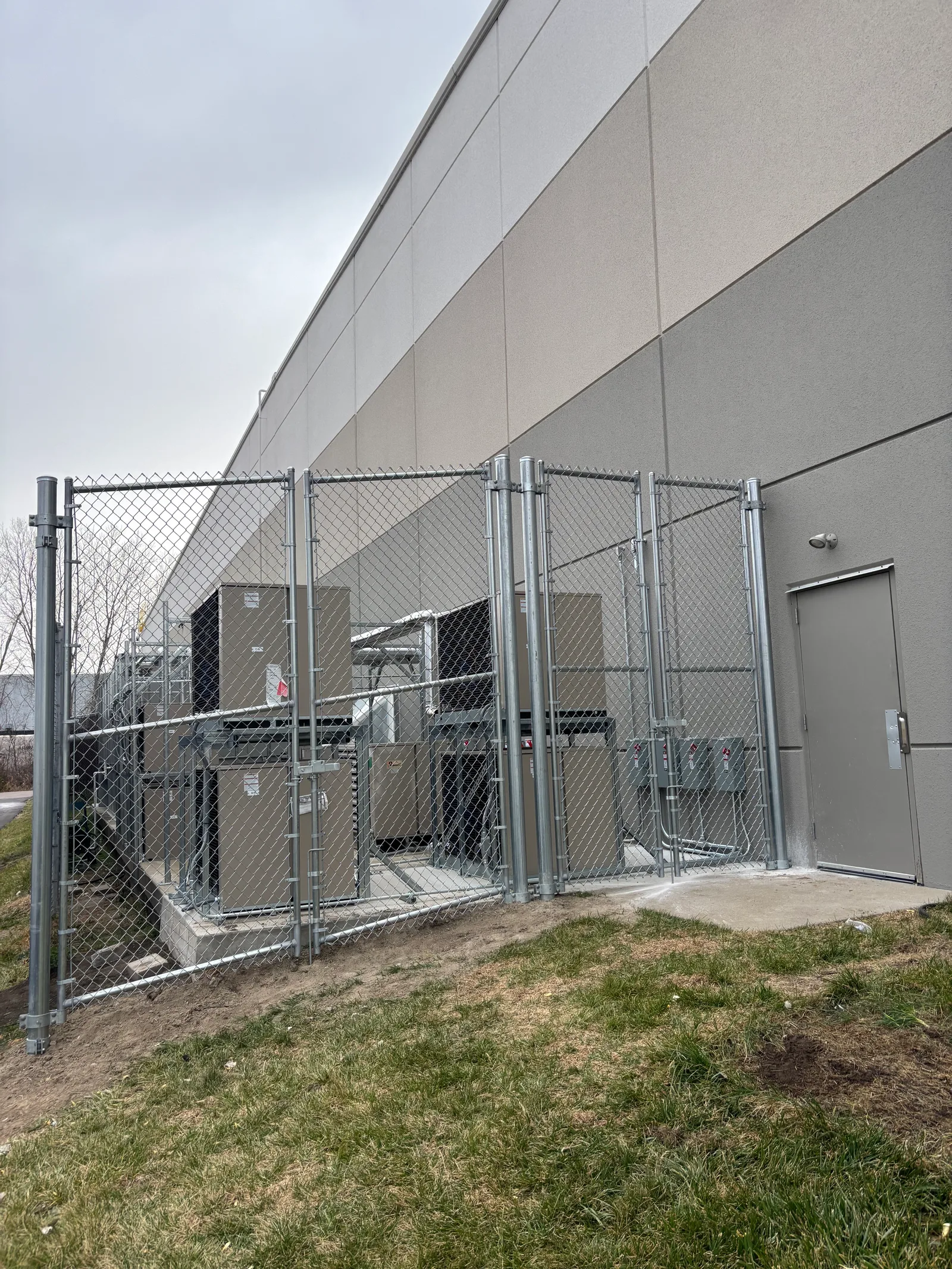 Galvanized chain link enclosure around HVAC and electrical equipment at a commercial property in Raymore, MO