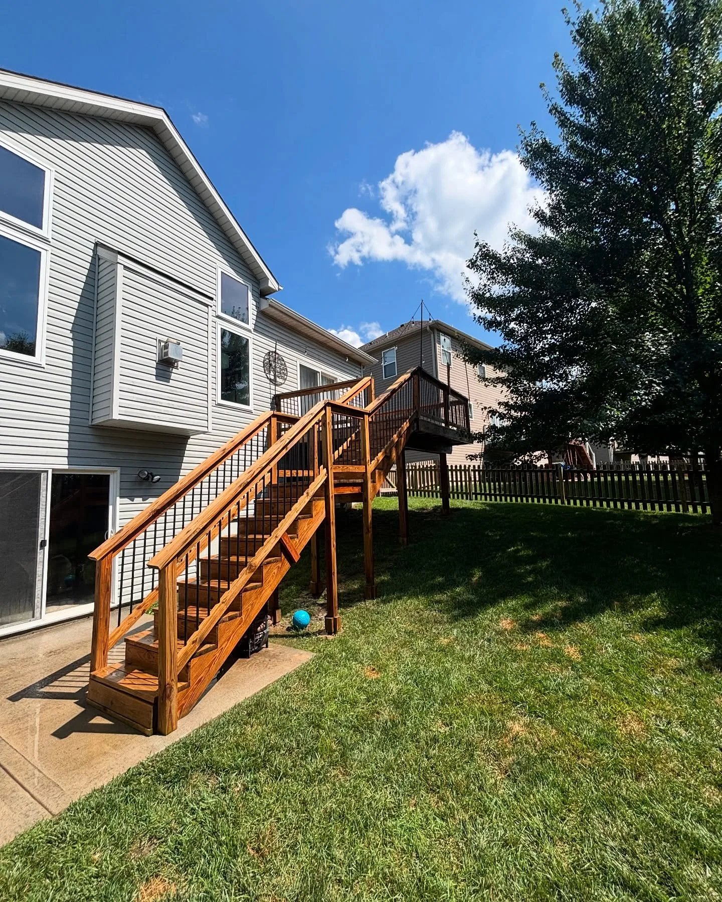 Elevated cedar deck with staircase freshly stained in Stilwell, KS — warm amber tone, sunny afternoon