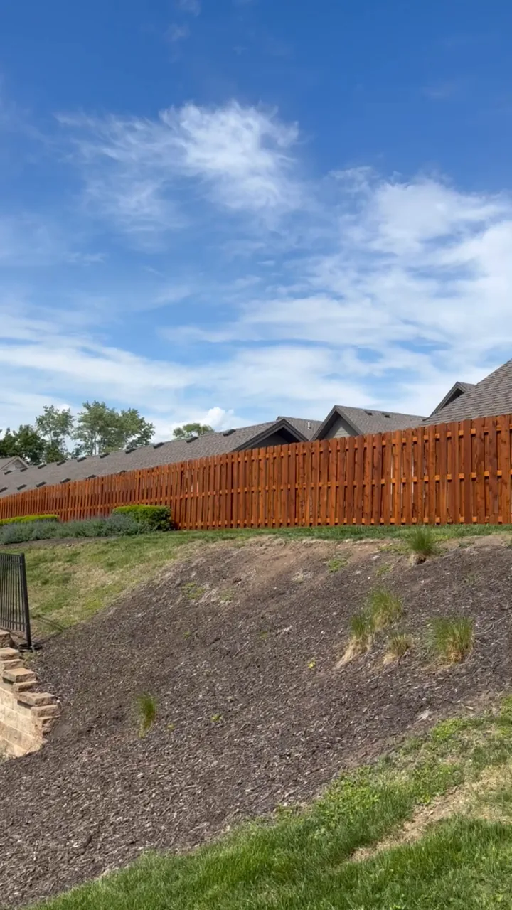 Freshly stained shadowbox wood fence above a sloped yard in Overland Park, KS — RKC Wood Care Pros