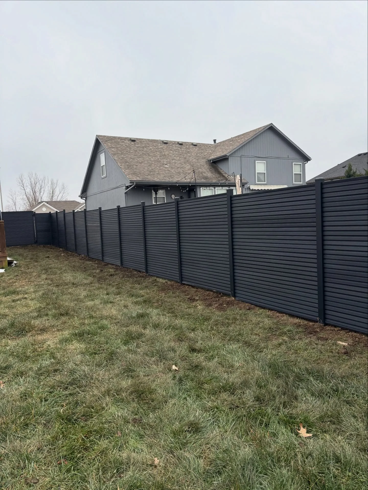 Long dark charcoal horizontal fence installation in Belton, MO — new construction neighborhood, overcast sky